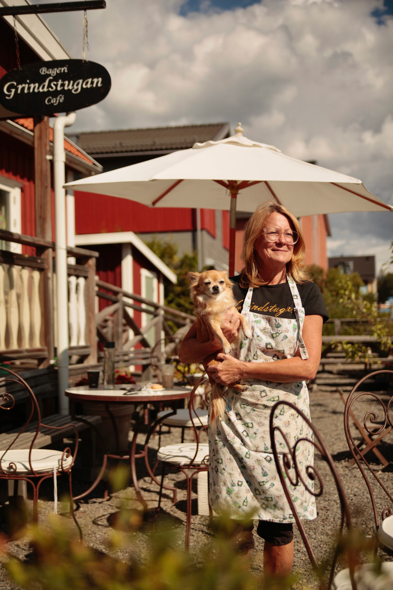 Glad medarbetare håller en liten hund på uteserveringen utanför Café Grindstugan i Tollare